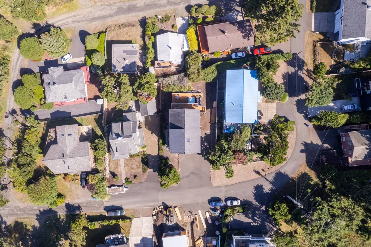 Wide shot of the front of the house, with a prominent extra-large driveway, landscaped yard, and neighboring homes visible. The welcoming scene suggests ample parking for RVs, boats, or ATVs, setting the stage for coastal adventures.