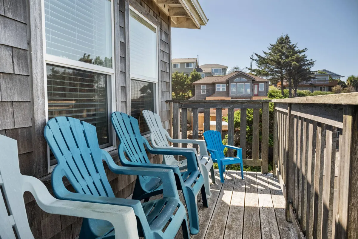 A group of blue adirondack chairs is arranged on a wooden deck overlooking neighboring homes, inviting guests to relax, socialize, and enjoy the surrounding views in a casual, welcoming atmosphere.