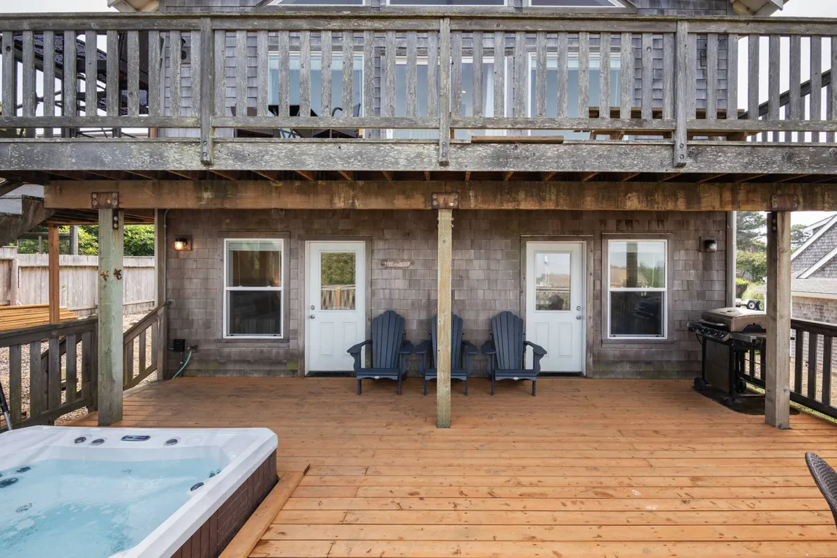 A welcoming deck features a bubbling hot tub surrounded by chairs and easy access to the house, set against the backdrop of an inviting outdoor space. The deck is ideal for relaxing after a day at the beach.
