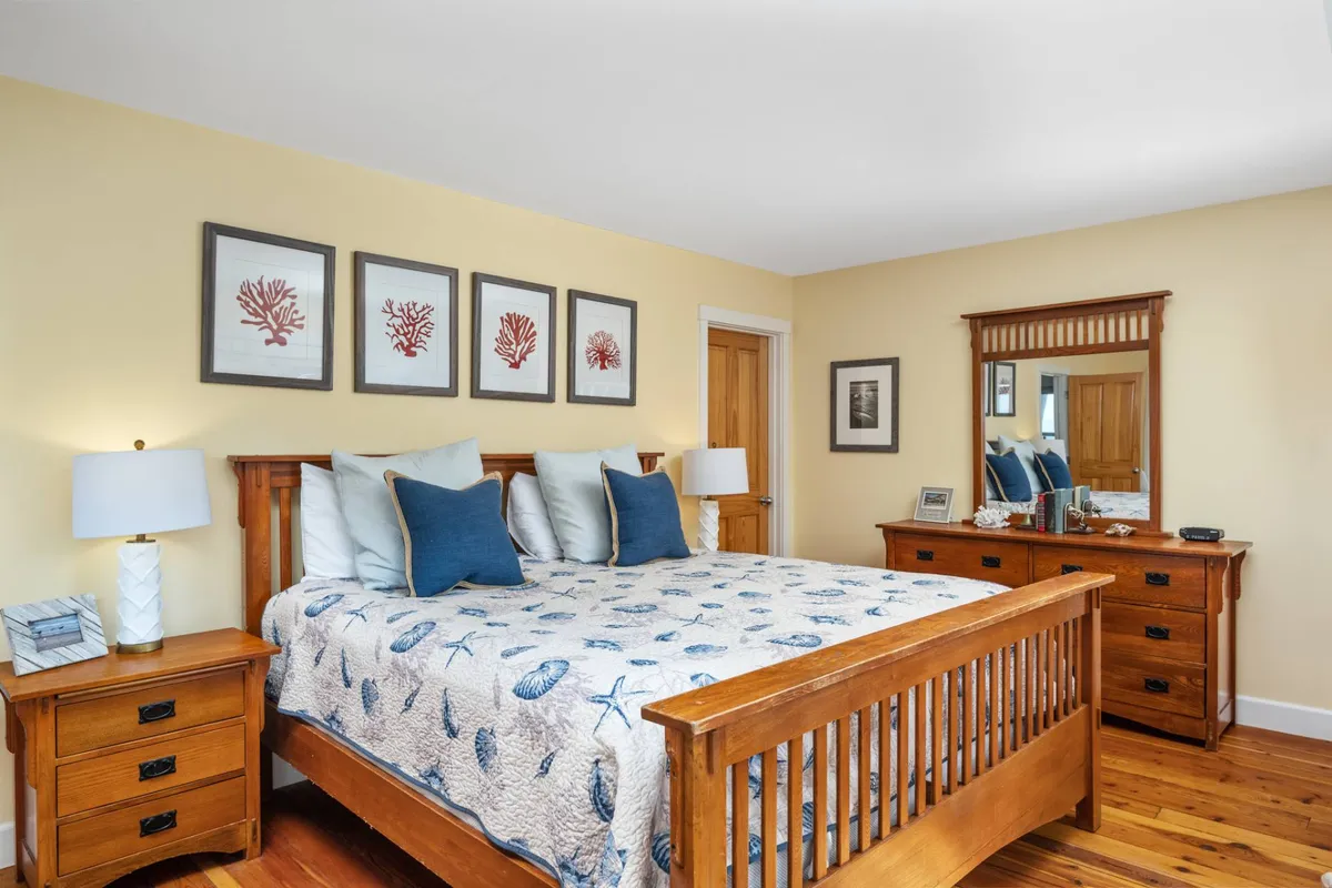 A calm, inviting bedroom featuring a bed with a decorative quilt, framed coral artwork above the headboard, and a wooden dresser. The atmosphere is serene, ideal for unwinding after a busy day.