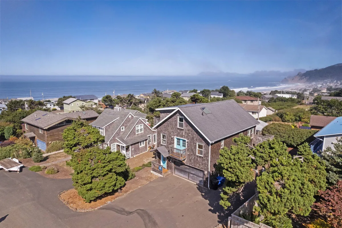 A two-story wooden house set amid trees, with an upper deck that offers ocean views. The home exudes a relaxed, beachy vibe, perfect for morning coffee on the porch or sunset viewing from the loft deck.