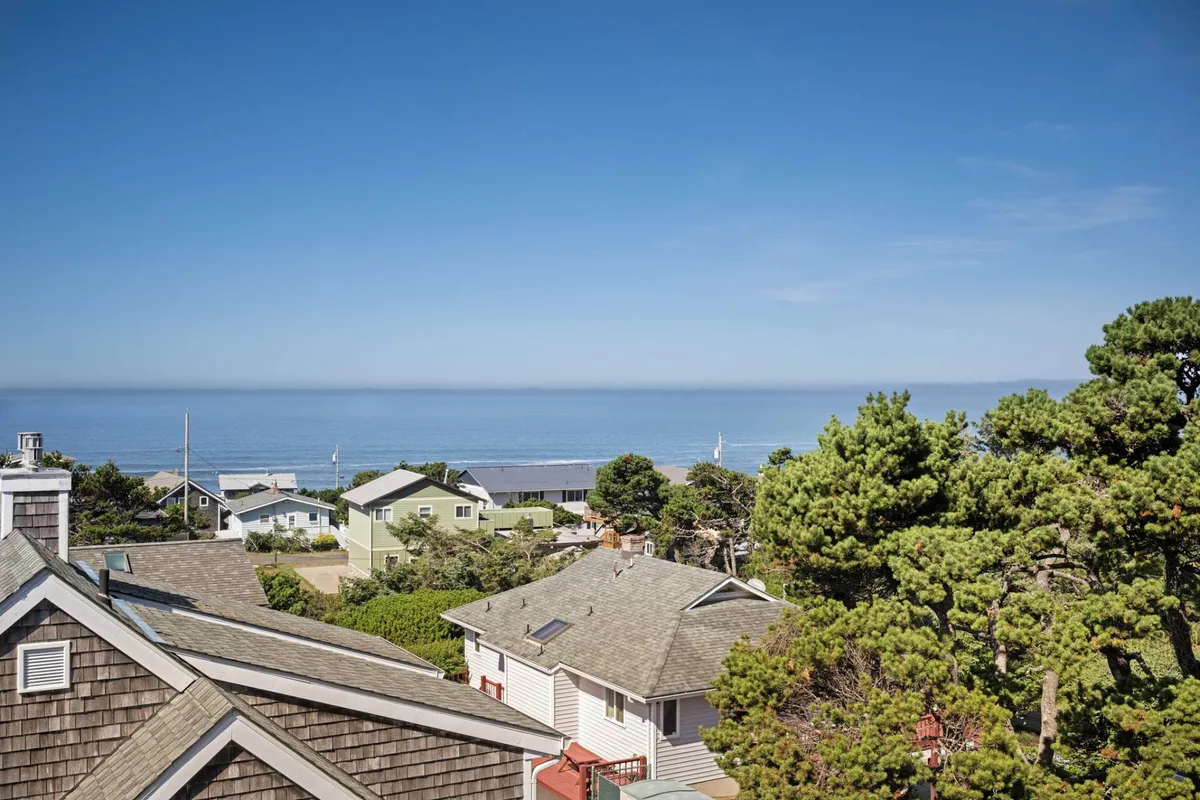 A tranquil view showing the ocean, neighboring houses, and leafy trees—perfectly conveying the natural beauty and proximity to beaches and attractions. The perspective is one of peaceful observation, suggesting exploration and serenity right outside the door.
