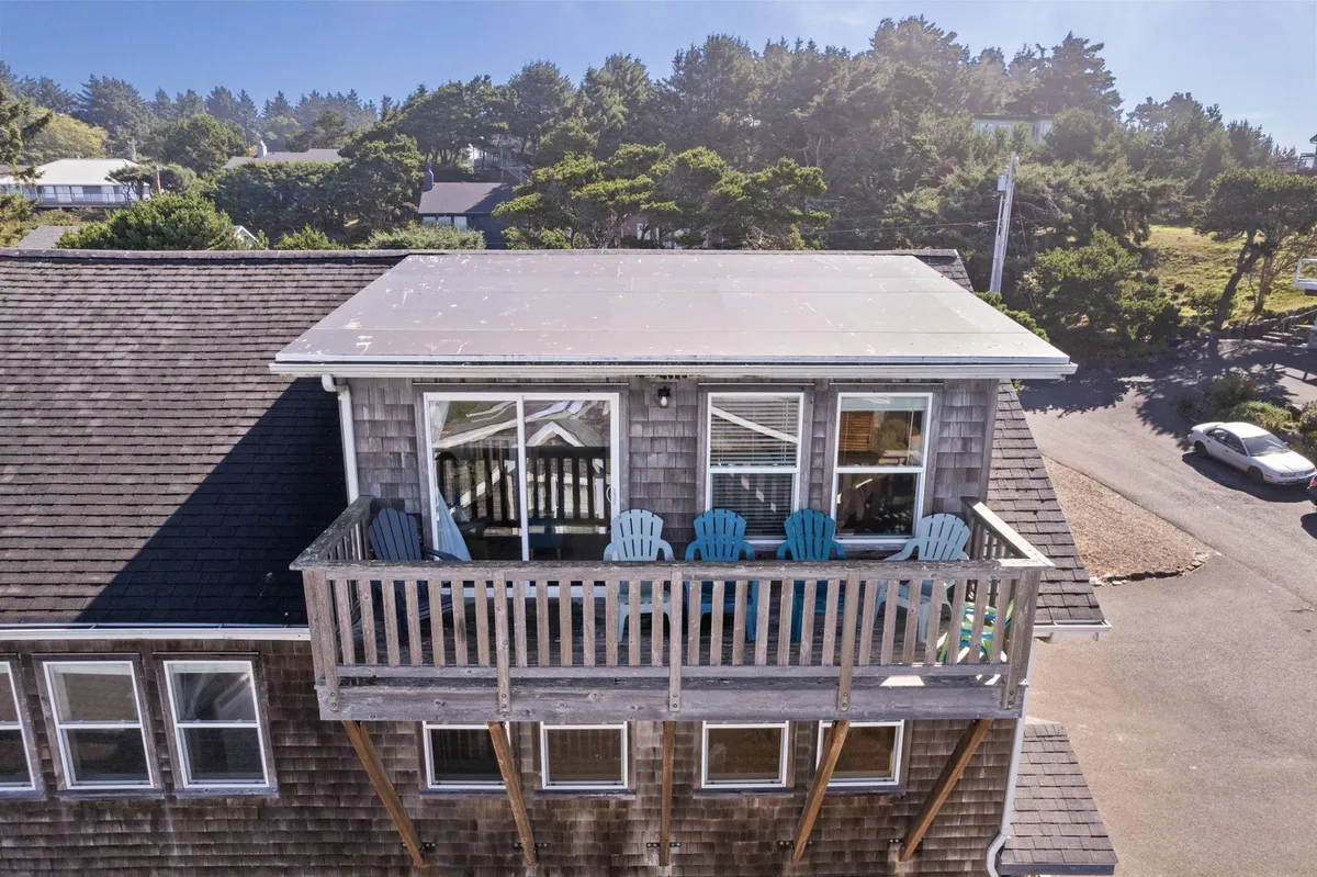 A welcoming exterior featuring a spacious balcony with Adirondack chairs, large windows, and ample sunlight. The scene suggests relaxation and social connection, offering views and outdoor comfort.