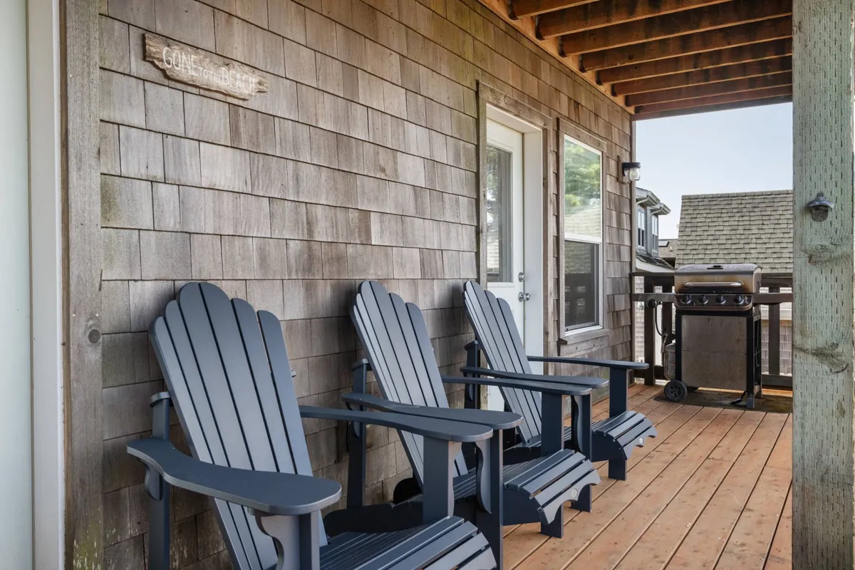 An inviting exterior shot showcasing Adirondack chairs set around a grill on a wooden deck, with the 'GONE FISHIN'' sign adding a playful touch. The arrangement hints at a space ideal for socializing, barbecuing, or relaxing after a day of local exploration.