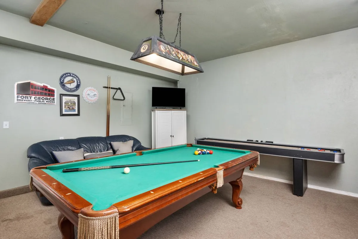 A lively game room featuring a pool table at the center, a comfortable sofa, a shuffleboard table along the wall, and colorful wall art. The space feels open and inviting, with plenty of room for friendly competition and group hangouts.