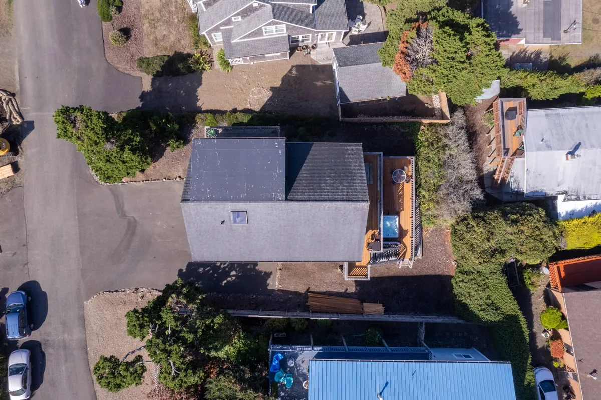 An exterior view featuring a calm rooftop deck surrounded by lush greenery and neighboring houses. The outdoor space is inviting, perfect for relaxing after beach walks or prepping for a trail adventure. The deck setting suggests a transition between home comfort and outdoor activities.